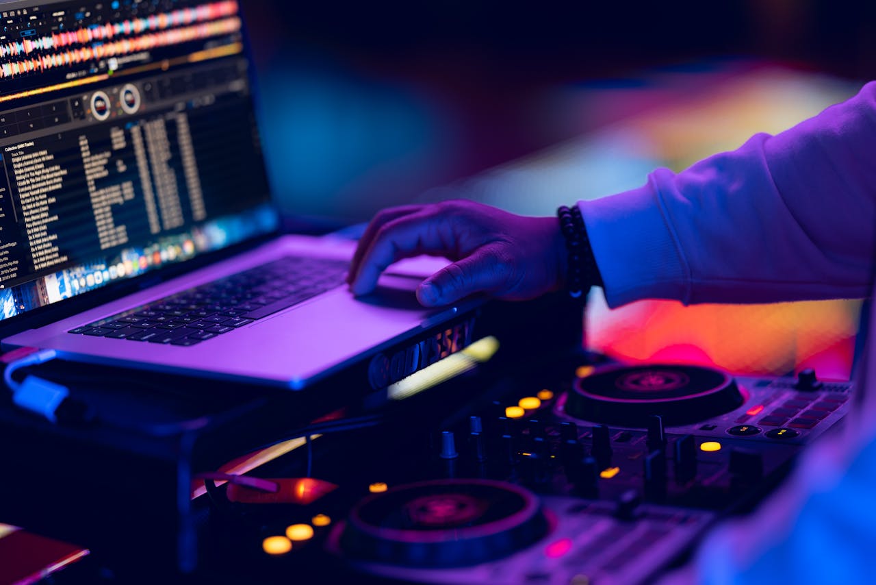 DJ adjusts music mix using laptop and mixer in vibrant nightclub setting.