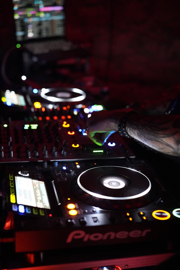 Close-up of a DJ's hands mixing music on a Pioneer turntable in a dimly lit nightclub.