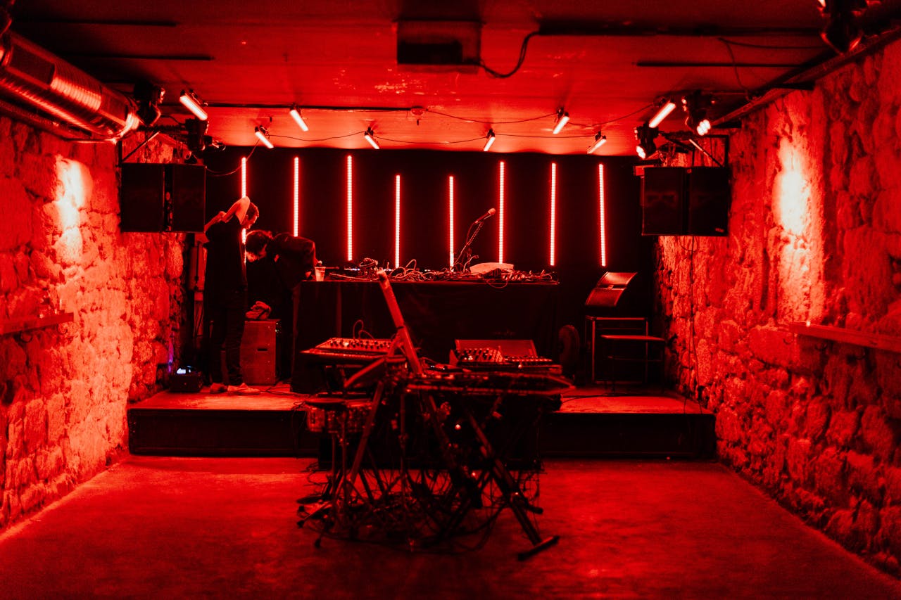 Underground electronic music venue with red lighting and DJ equipment, captured at night.